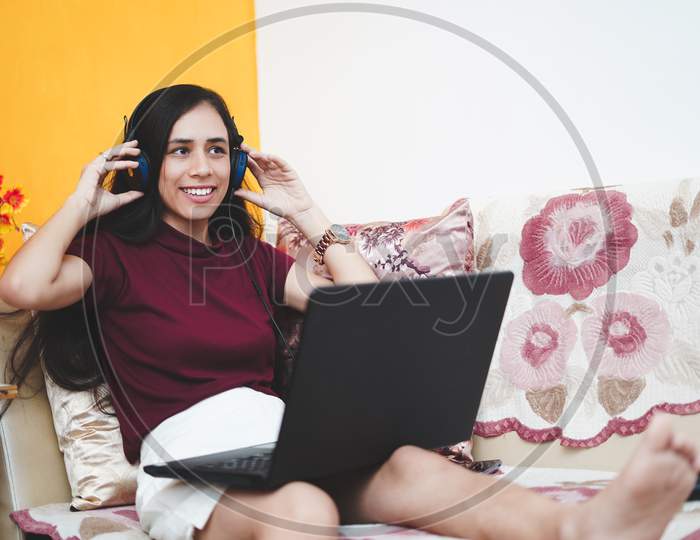 A Young Beautiful Indian Girl Wearing Headphones While Working On Her Laptop, Happy And Cheerful While Working From Home.