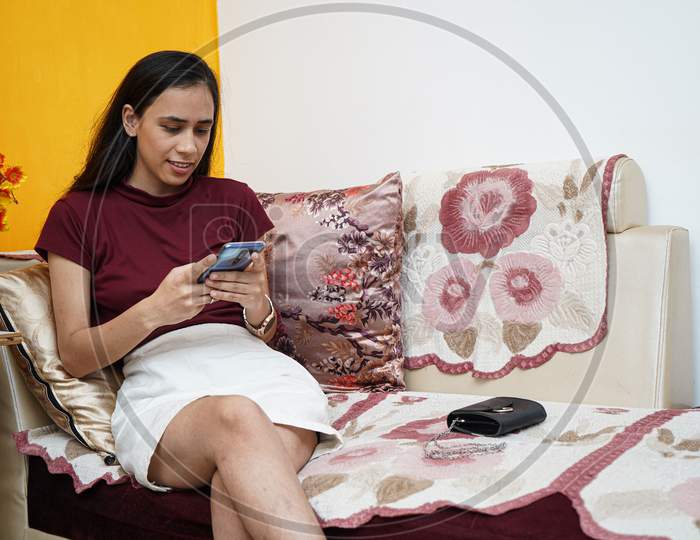 A Young Indian Girl Using Her Phone While Sitting On The Sofa At Home.