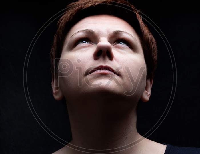 Portrait Of Short Hair Woman Looking Upward Against Black Background.