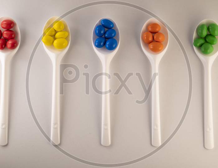 colorful chocolate balls on white  spoons on a white background.