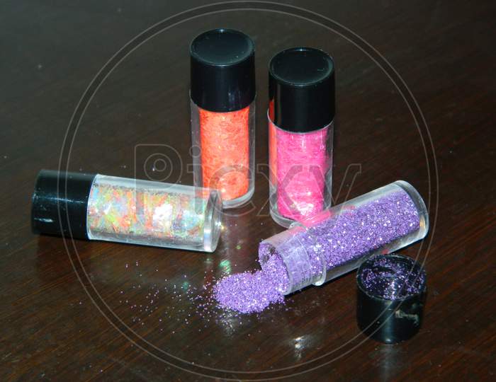 Four different colored glitters in the small containers.Colourful glitters in which one is fallen