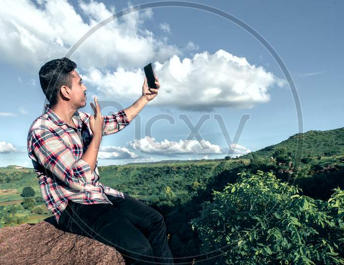 man taking selfie seating on top of hill stone