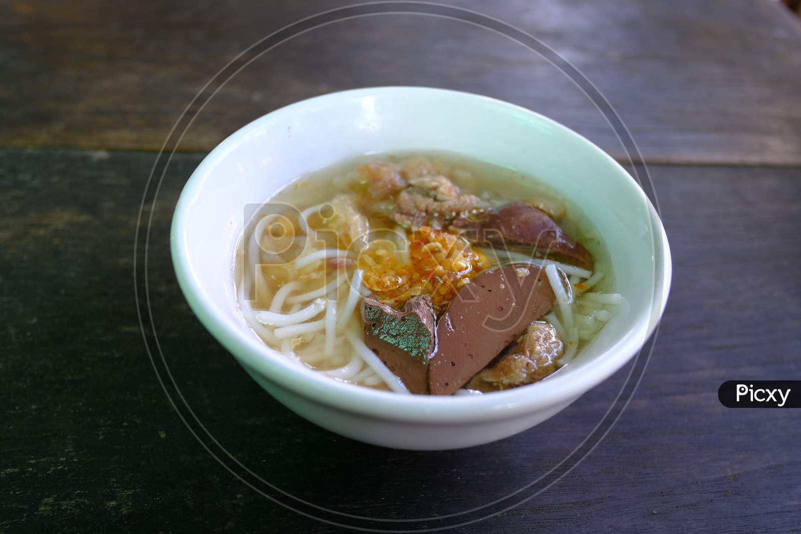 Mini Bowl Of Steam Thai Rice Vermicelli With Pig Blood In Clear Soup Topped With Fried Garlic On The Dark Wooden Table