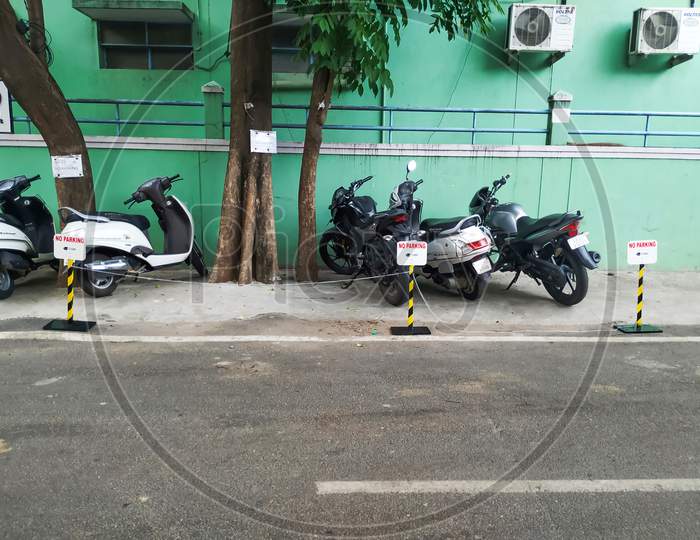 Closeup of Two Wheeler or Bikes Parking near the compound of the building with no parking metal stand for other than companies.