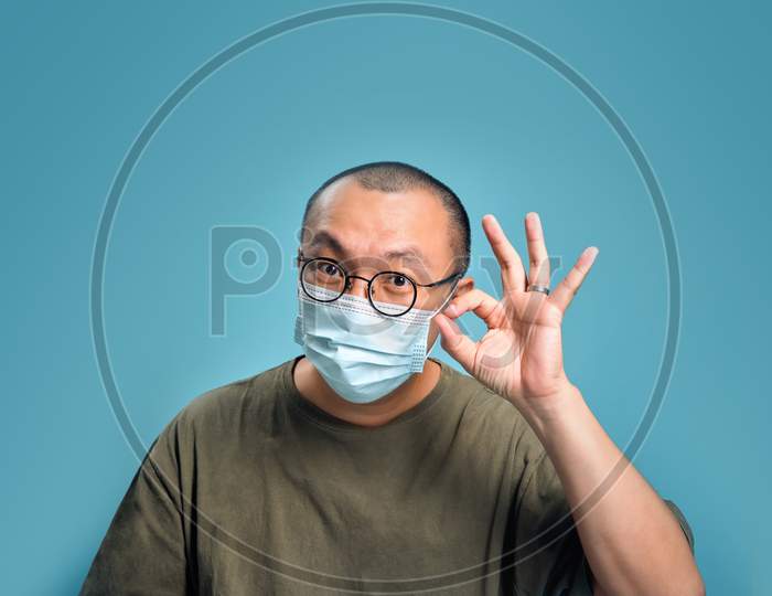 Young Asian Man Wearing Respirator Mask To Protect himself from Virus Outbreak And Feeling Positive On Blank Background. New Virus Outbreak That Alerts The World Health Concept, Empty Space Isolated On Blue.