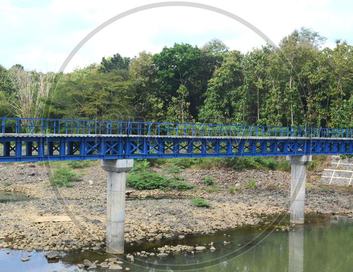 Long Blue Iron Bridge With Two Pillars On The River