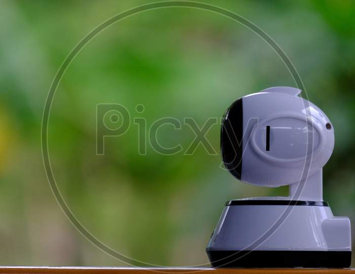 A White Modern Indoor Cctv Camera With Internal Infrared Is Rotating To Check Home Security With Wireless Connection Via Smartphone'S Application By Internet Ip Controlled With Blurred Background