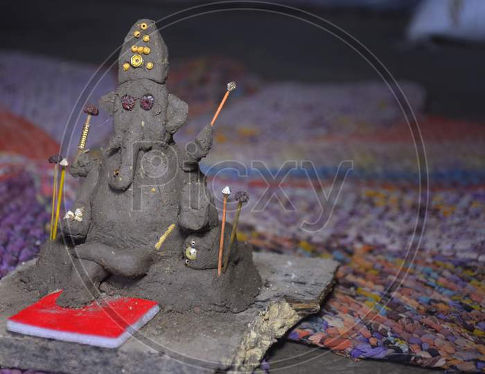 Lord Ganesha In Selective Focus, Made Of Clay With Colorful Blur Background, In Indian Village