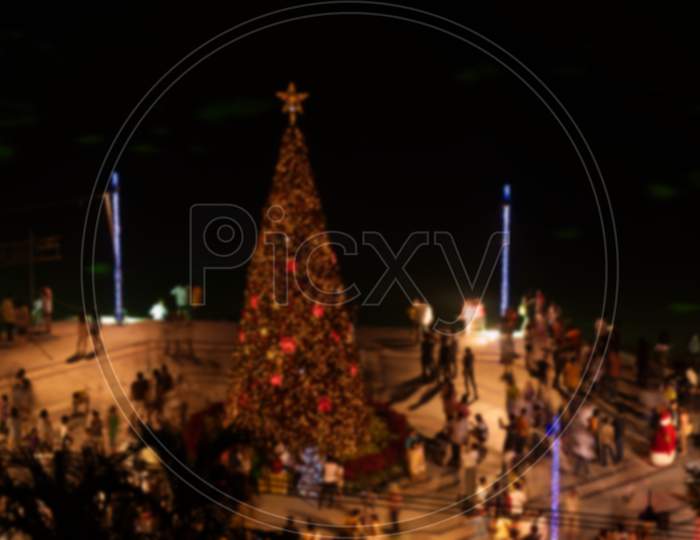 Blur Image Of Asian People Celebrating Christmas Party Or New Year Festival Around Christmas Tree In The Open Space By The River At Night