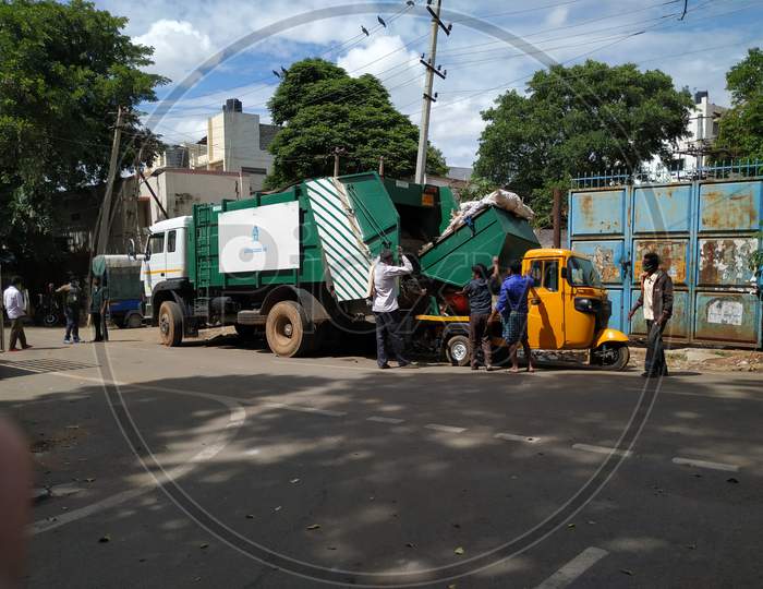 Closeup of Garbage Collecting Workers working to Unload Waste from Auto to Lorry in a Roadside.