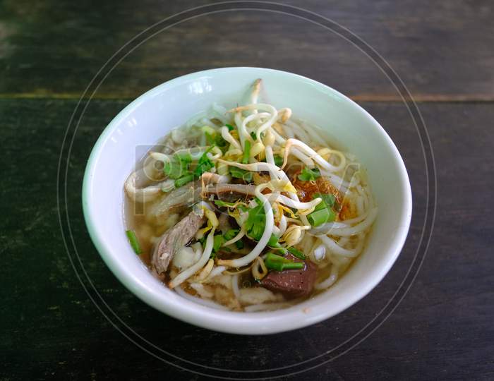 Mini Bowl Of Steam Thai Rice Vermicelli With Pig Blood In Clear Soup Topped With Fried Garlic; Bean Sprouts; Coriander And Spring Onion On The Dark Wooden Table