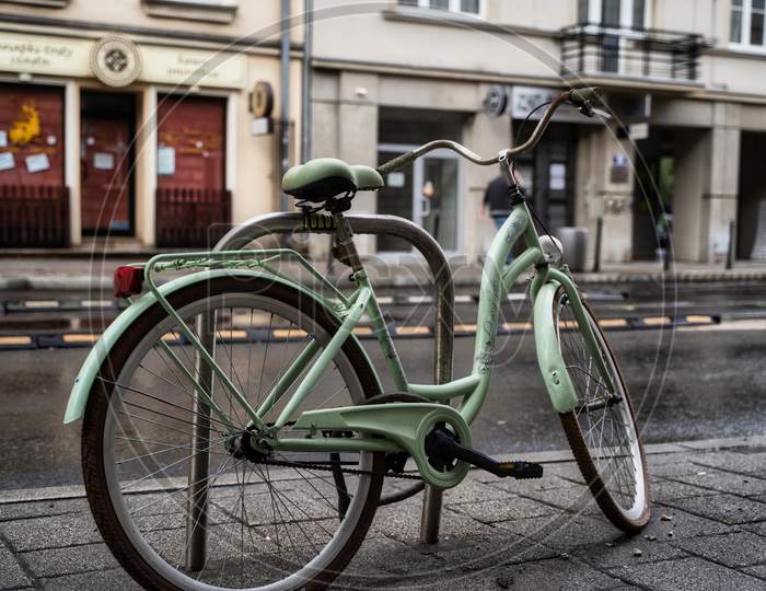 Krakow, Poland - July 18, 2020: A Closeup Of A White Bicycle Parked Next To Busy Street In Krakow In Rainy Weather
