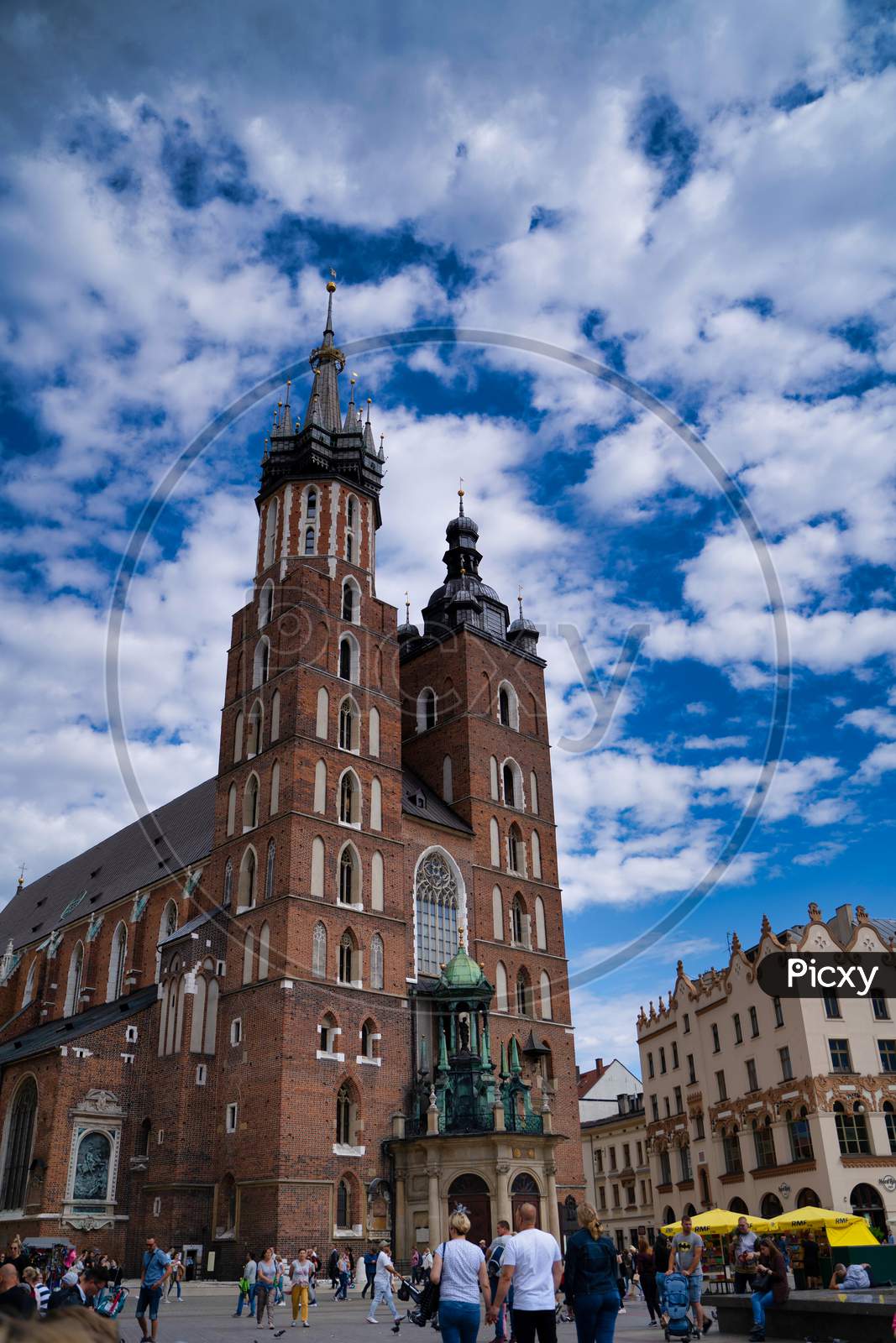 Krakow, Poland - July 12, 2020: Vertical Shot Of Saint Mary’S Basilica Is A Brick Gothic Church Adjacent To The Main Market Square Against Dramatic Cloudy Blue Sky