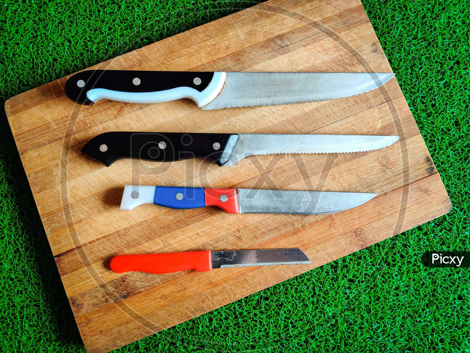 Four Colored Different Sizes Of Knives Kept On Chopping Board.