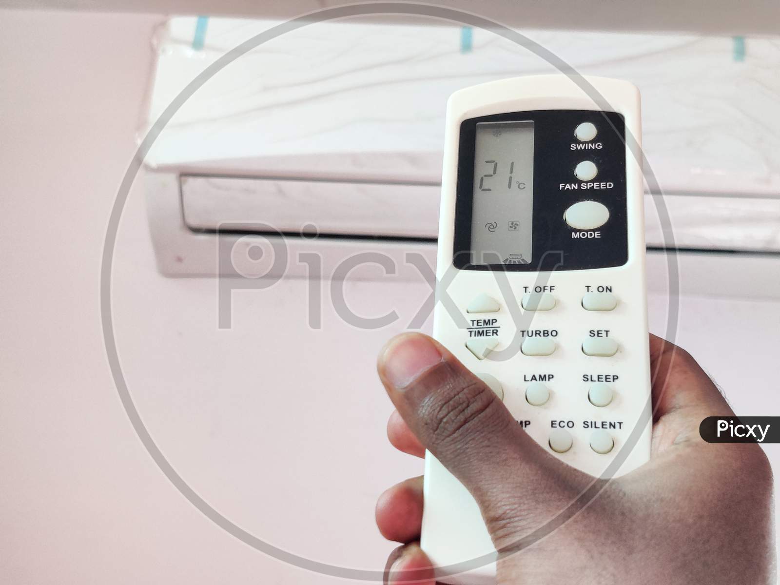 Indian Man Adjusting Temperature Of Air Conditioner By Remote In Room. Setting 21°C Temperature.