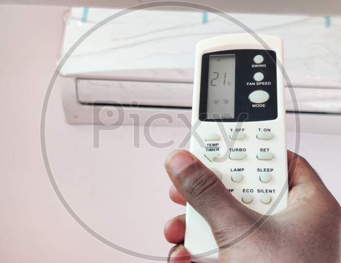 Indian Man Adjusting Temperature Of Air Conditioner By Remote In Room. Setting 21°C Temperature.