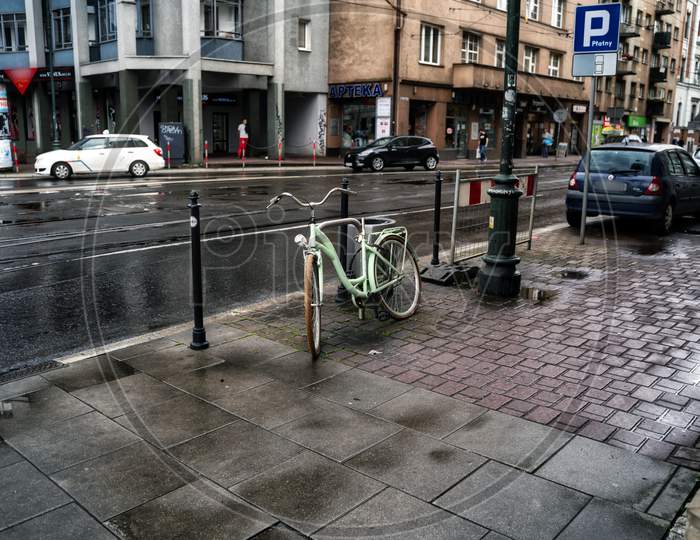 Krakow, Poland - July 18, 2020: A Wide Angle Shot Of A White Bicycle Parked Next To Busy Street In Krakow In Rainy Weather
