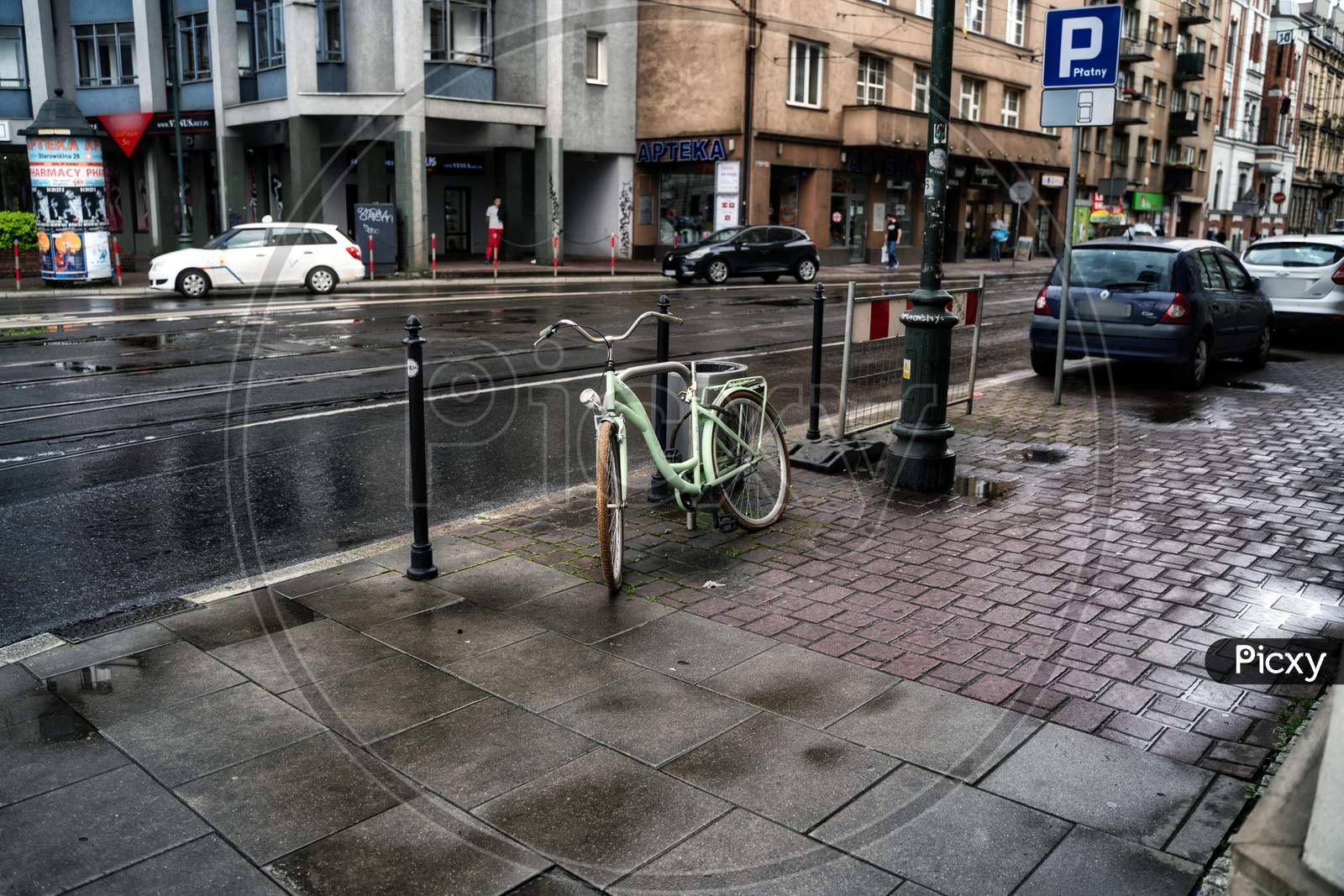 Krakow, Poland - July 18, 2020: A Wide Angle Shot Of A White Bicycle Parked Next To Busy Street In Krakow In Rainy Weather