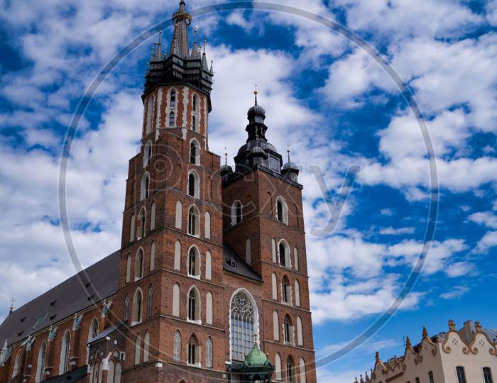 Krakow, Poland - July 12, 2020: Vertical Shot Of Saint Mary’S Basilica Is A Brick Gothic Church Adjacent To The Main Market Square Against Dramatic Cloudy Blue Sky