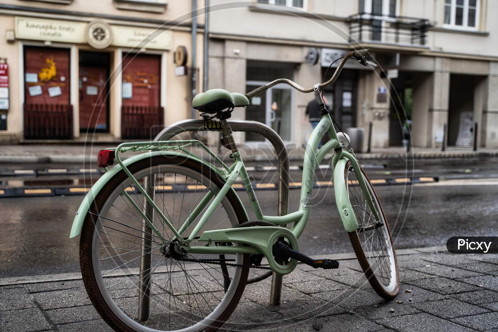 Krakow, Poland - July 18, 2020: A Closeup Of A White Bicycle Parked Next To Busy Street In Krakow In Rainy Weather