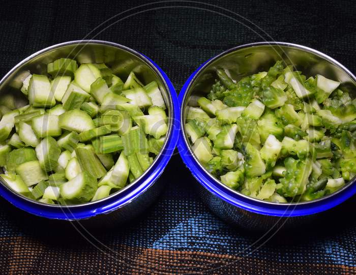 Fresh Bitter Gourd And Okra Fruits Pieces In Two Bowls,