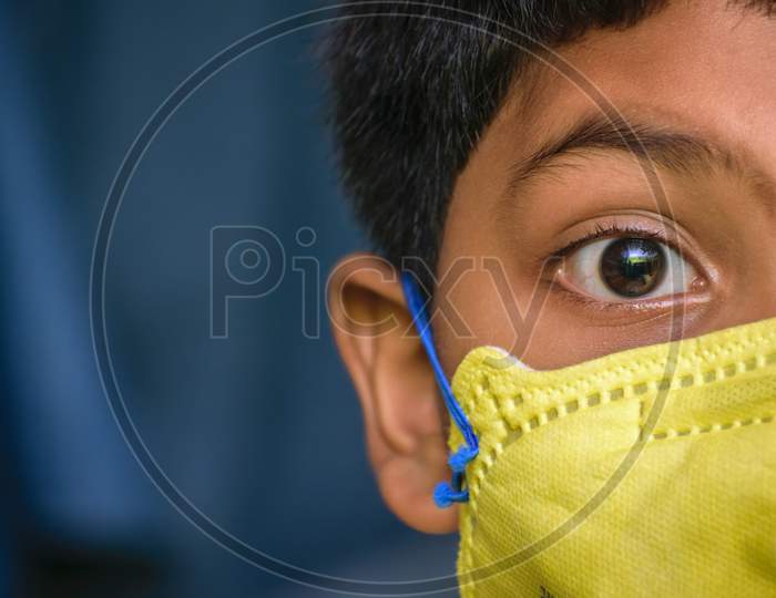 Isolated Young Indian Boy With Prominent Eyes Wearing N95 Face Mask For Protection Against Covid 19. Space For Text In Left