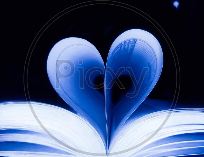 Blue Heart,Heart shape or love symbol against pages of books with blue lighting effect and black background.
