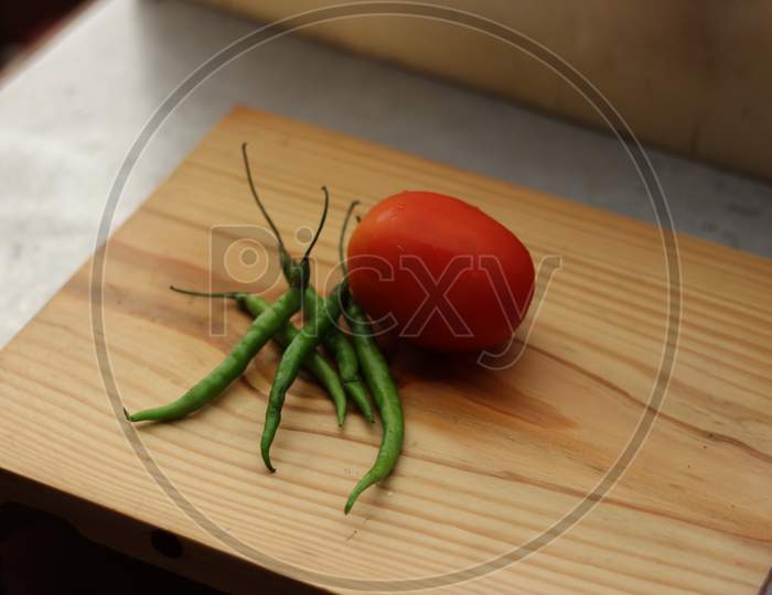 Green chillies and Tomato isolated on wooden board, ready to cut