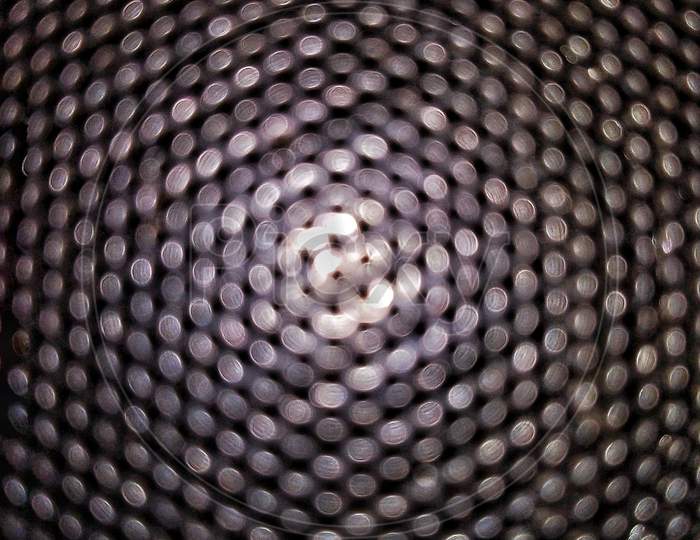 A Black Shinny Round Pattern Grill On Which White Light Is Flashing At Centre