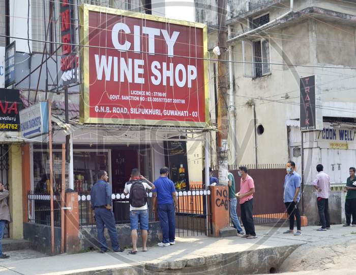 People maintain social distance as they stand in a queue outside a wine shop