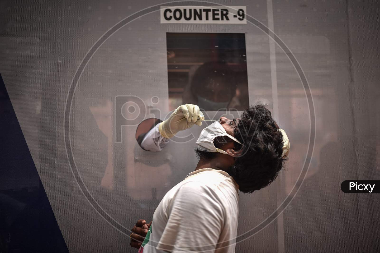 A medic takes a swab sample of a man for the COVID-19 test from a swab collection bus in Vijayawada.