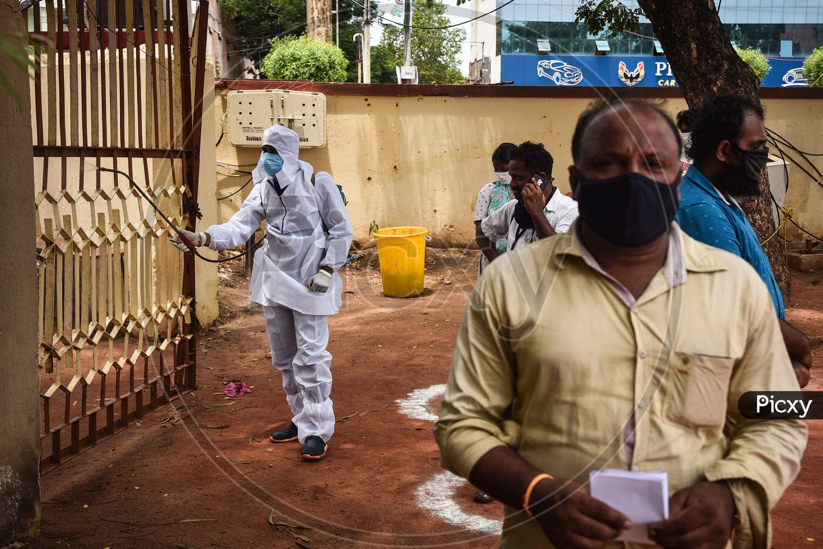 A corporation worker sanitizes the area as people wait for the COVID-19 test in Vijayawada.
