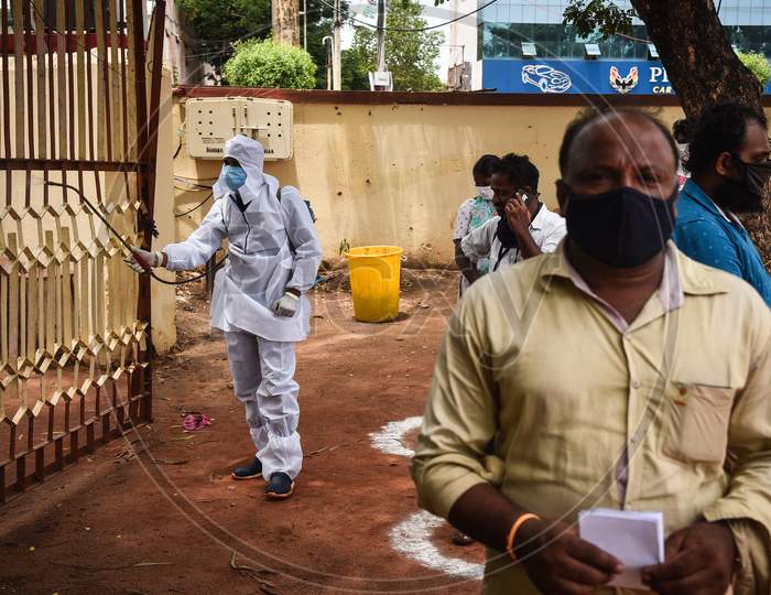 A corporation worker sanitizes the area as people wait for the COVID-19 test in Vijayawada.