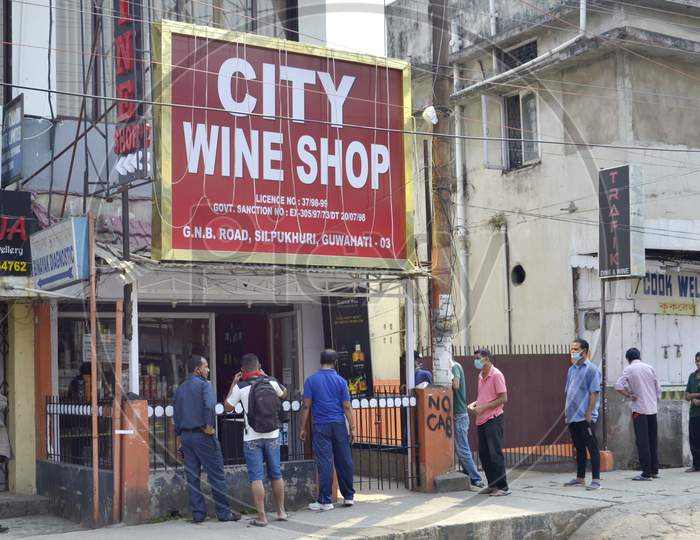 People maintain social distance as they stand in a queue outside a wine shop