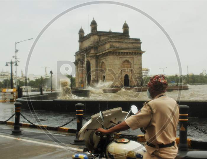 A Police personnel rides past, as the waves crash at the Gateway of India during high tide in Mumbai, India on July 6, 2020.