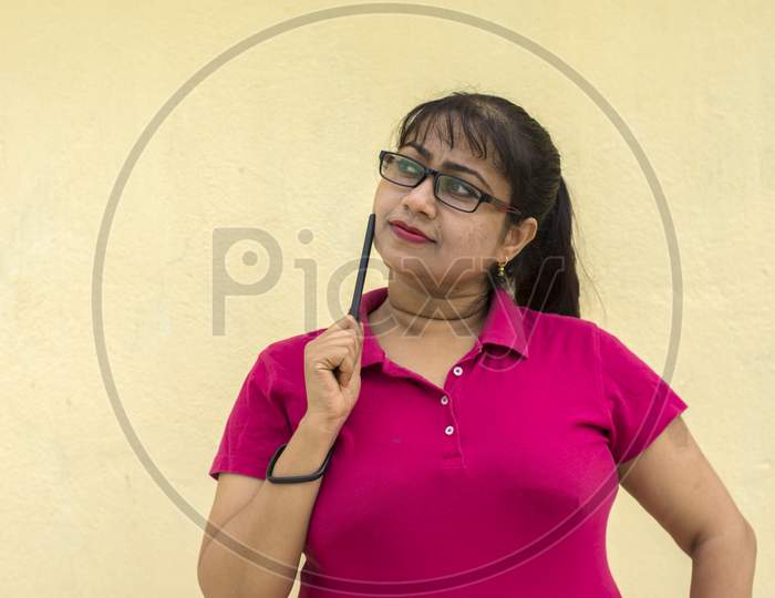 Indian Female Model Looking Straight Happily With Slight Smiling Face A Pen In Her Hand In Yellow Background With Copy Space For Text