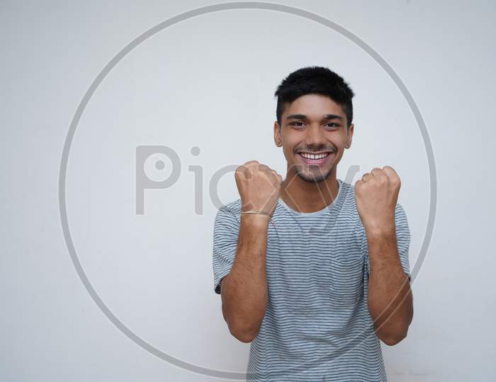 Hurray And Cheers. Portrait Of Young Handsome Indian Model Looking Excited While Standing Against White Background
