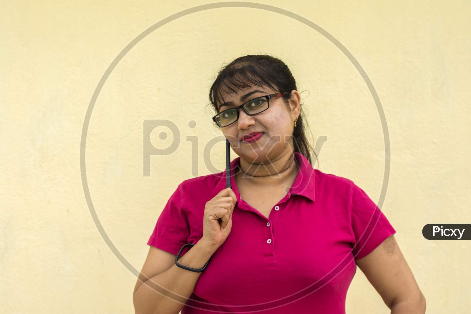 Indian Female Model Looking Straight Happily With Slight Smiling Face A Pen In Her Hand In Yellow Background With Copy Space For Text
