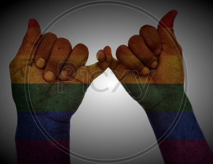 man hands holding each other by fingers on pattern rainbow flag symbolising gay love.