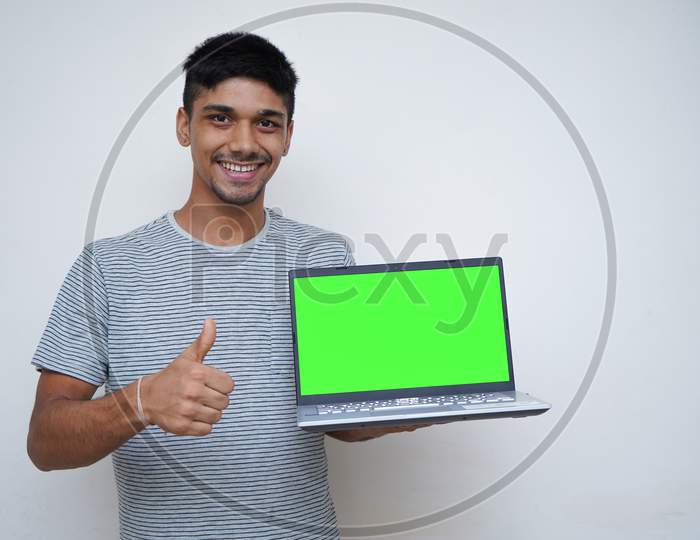 Young Handsome Asian Teen Boy Showing Thumbs Up With A Laptop On The Other Hand With A Green Screen.