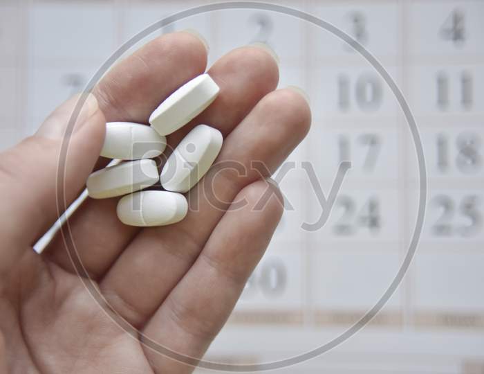 Selective Focus At The Hand And Pills With The Blurred Calendar At The Background