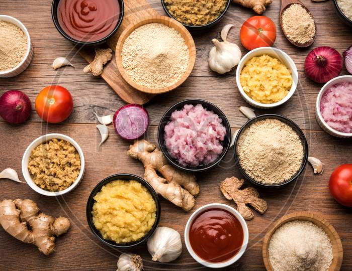 Ginger, Garlic, onion and tomato paste and powder in and raw form. Group of Basic Indian food ingredients over wooden background
