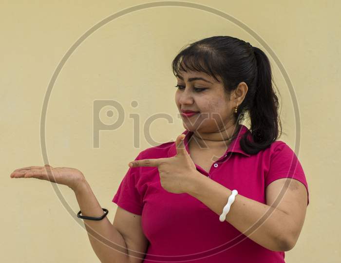 Indian Female Model Looking Right Side Pointing Her Plum With Finger In Yellow Background With Copy Space For Text