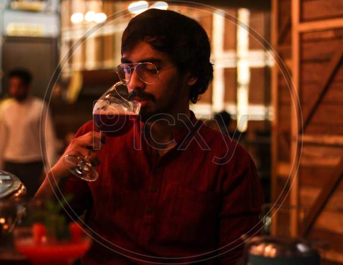 Young Man Drinking Red Wine At A Cafe Indoors With Colorful Lights All Around Him.