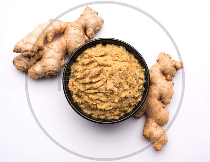 Fresh mashed Ginger / Adrak paste in white bowl with raw ginger over white background