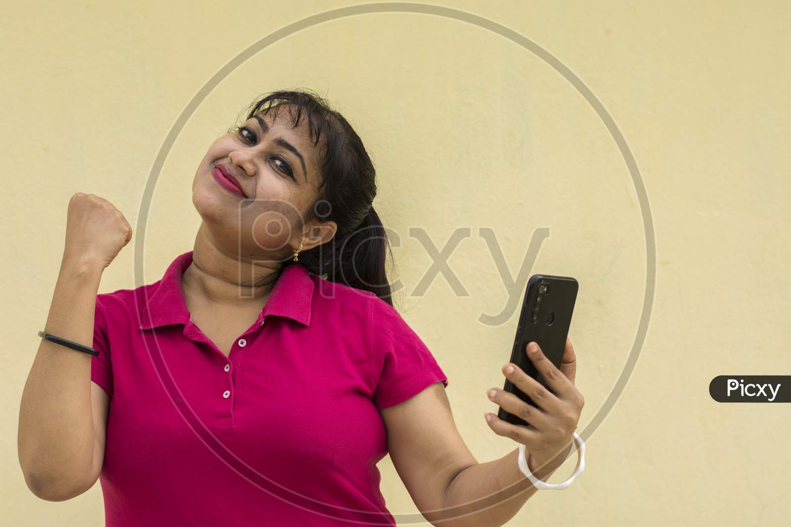 Indian Female Model Looking At Mobile Phone Happily With Slight Smiling Face In Yellow Background With Copy Space For Text
