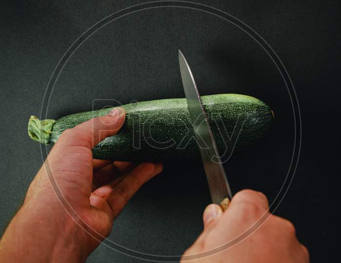 Two Hands Cutting A Cucumber With A Long Knife