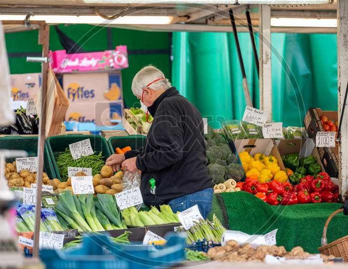 A Mature Man With Hearing Aid Wearing A Protective Face Mask Shopping At An Outdoor Fruit And Veg Market Stall