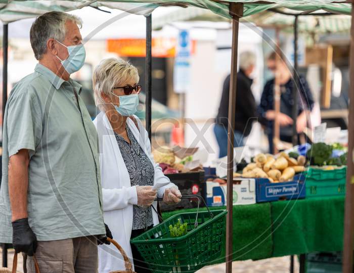A Mature Couple Wearing Protective Face Masks Shopping At An Outdoor Fruit And Veg Market Stall