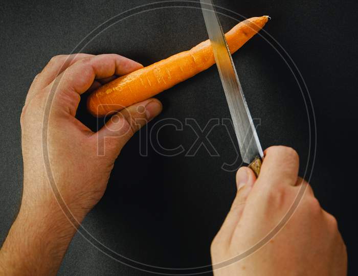 Two Hands Cutting A Carrot With A Long Knife